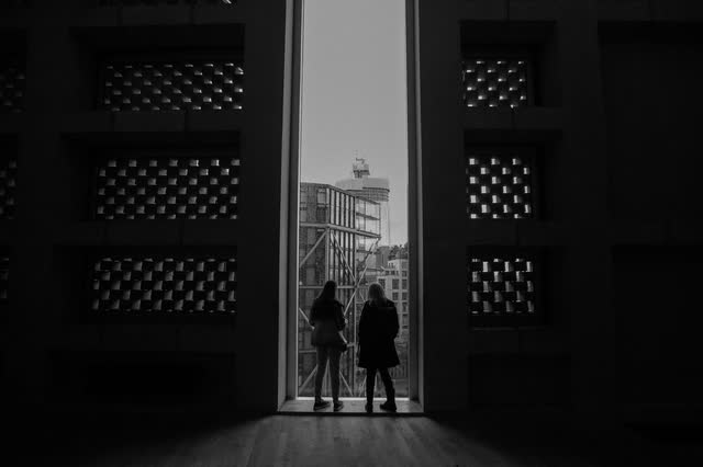 Two people standing in a tall dark doorway, looking out at a city