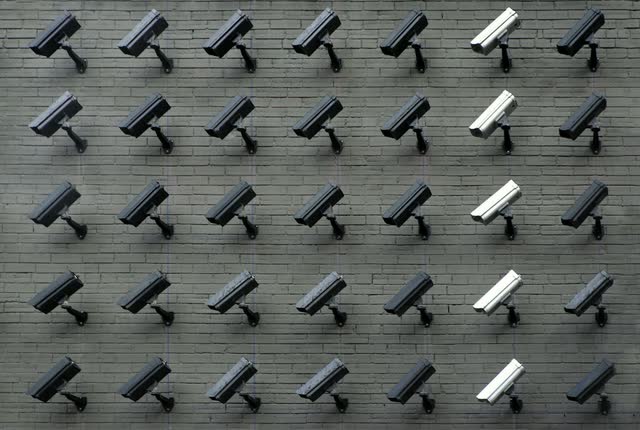 Rows of security cameras mounted on a grey wall, all pointing the same way