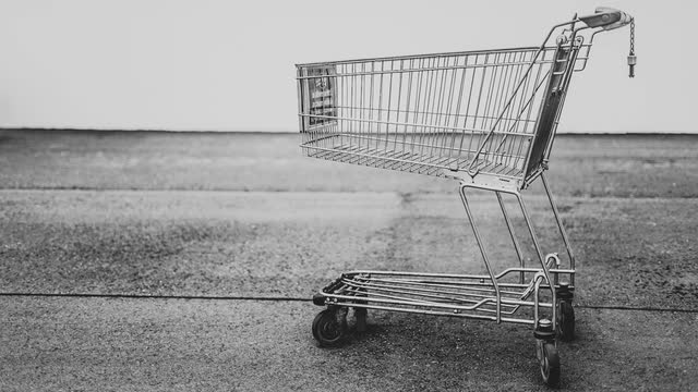 An empty shopping cart standing alone on bare pavement, in black and white